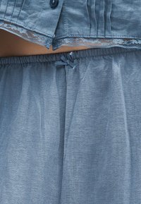 Μπλε ρούχο από ύφασμα με δαντέλα, λεπτομέρεια με κουμπί και ελαστική μέση με μικρό φιόγκο δεμένο μπροστά.