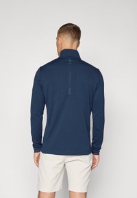 Marineblauwe performance shirt met lange mouwen en hoge kraag, voorzien van een uniek rugpaneelontwerp en textuuraccenten in de stiksels.
