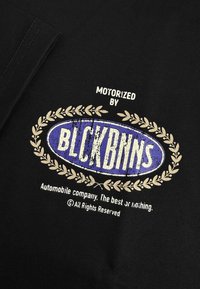 Zwarte stof met een centraal ovaal logo in blauw met witte tekst "MOTORIZED BY BLCKBNNS" en decoratieve gouden laurieraccenten.