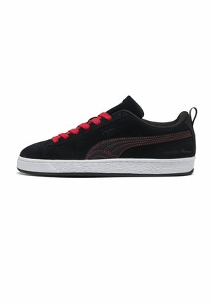 Baskets basses noires avec lacets rouges et coutures, semelle blanche texturée et languette au talon sur fond blanc.