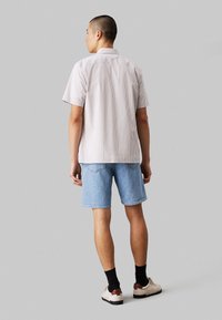 Camicetta a maniche corte con bottoni, a righe verticali chiare e scure, abbinata a pantaloni corti in denim azzurri e sneakers neutre.