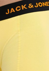 Sárga boxer alsónadrág fekete derékkal, amelyen narancssárga betűkkel szerepel a "JACK & JONES" felirat. Puha anyag, sima textúrával és megerősített varrással.