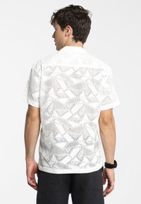 Witte T-shirt met korte mouwen, voorzien van een geometrisch uitgesneden ontwerp met een textuurpatroon, gedragen door een mannelijk model vanuit een achteraanzicht.