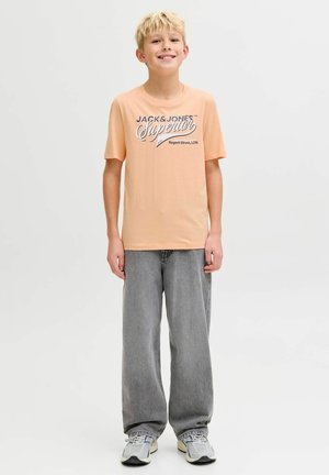 Virspuidust aprikoosikarva T-särk sinise "JACK & JONES Superior" graafilise mustriga, sobitatud halli lahtiste teksade ja hallide spordijalatsitega.