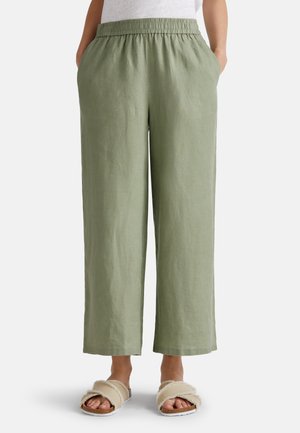 Pantaloni larghi in lino verde chiaro con elastico in vita, tasche laterali e una texture liscia, abbinati a sandali beige in peluche da indossare facilmente.