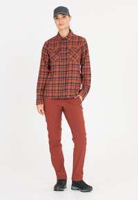 Röd och svart rutigt skjorta med två bröstfickor, ihopparad med tajta, stretchiga rostfärgade byxor och svarta vandringsskor.