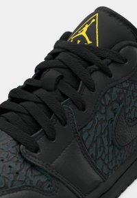 Sneaker nera con pelle texturizzata a motivo screpolato, lacci neri e logo Jumpman giallo sulla linguetta.