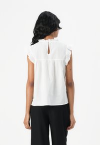 Blouse blanche à manches courtes froncées avec un design à dos en trou de serrure et une texture douce, associée à un pantalon large noir.