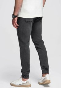 Pantalones de chándal grises de mezclilla, con puños elásticos, bolsillos traseros y un corte ajustado. Llevados con zapatillas blancas.
