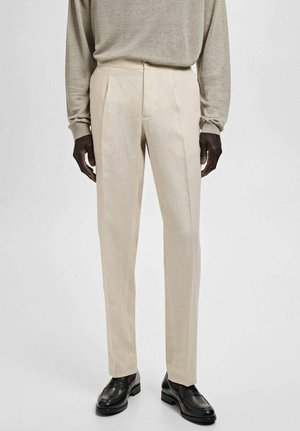 Beige maßgeschneiderte Hose mit leichtem Glanz, flacher Vorderseite, zwei Seitentaschen und geradem Bein, kombiniert mit schwarzen Slippern.