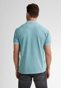 Světle modrá polo košile s krátkým rukávem, zakřiveným hřbetním švem, texturovanou tkaninou a žebrovaným límečkem. Nošena s tmavými džíny.