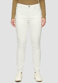 Witte skinny jeans met een gladde textuur, vijf zakken en een knoopsluiting. Gemaakt in combinatie met witte sneakers en een bruin shirt met lange mouwen.