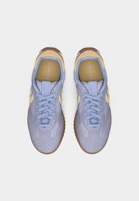 Ζευγάρι παπουτσιών Converse σε ανοιχτό μωβ και μπεζ με υφασμένο ράψιμο και λαστιχένιες σόλες σε καραμέλα, φωτογραφημένα από πάνω σε λευκό φόντο.