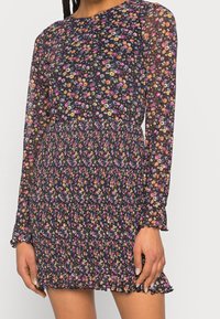 Černé květinové šaty s dlouhými průsvitnými rukávy, s nabíraným pasem a volánovou spodní částí. Na látce jsou po celé ploše pestré květiny.