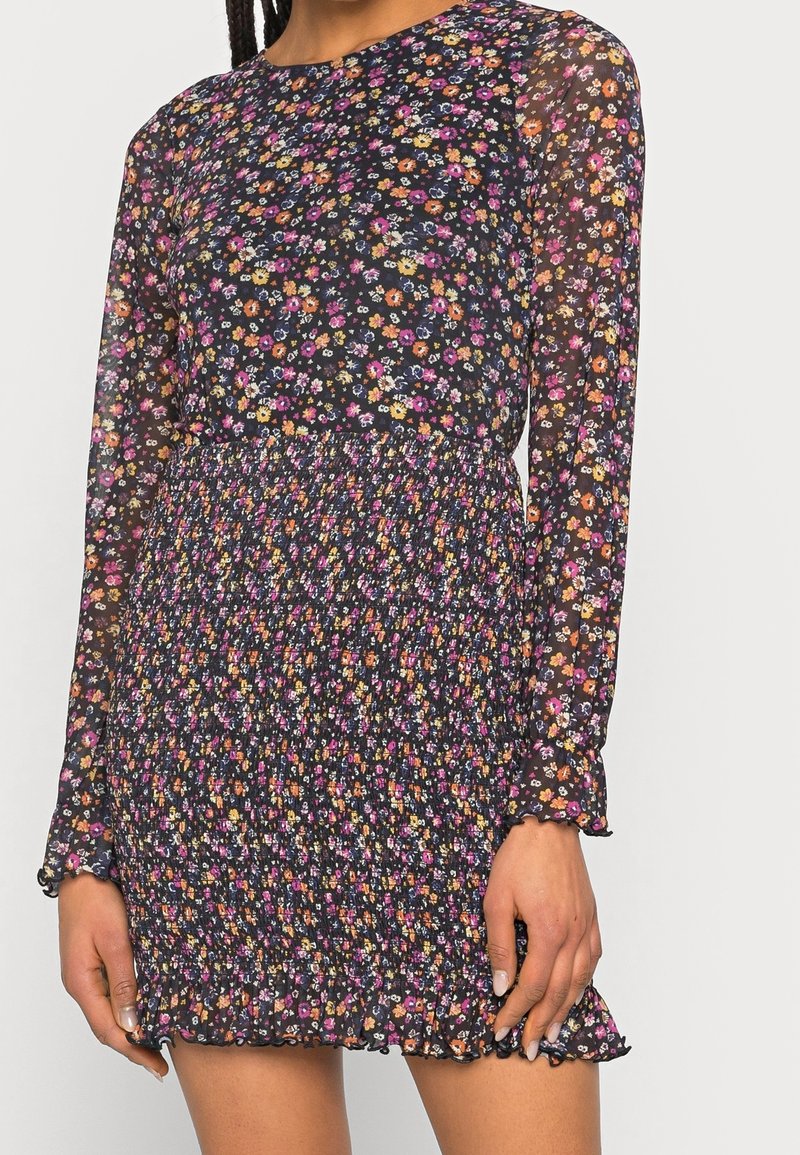 Černé květinové šaty s dlouhými průsvitnými rukávy, s nabíraným pasem a volánovou spodní částí. Na látce jsou po celé ploše pestré květiny.