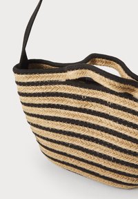 Sac en paille tissé présentant des rayures naturelles et noires alternées, une ouverture sur le dessus et de courtes poignées. La finition texturée ajoute de la dimension.