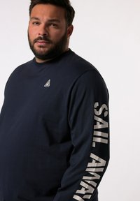Maglietta a maniche lunghe blu navy realizzata in tessuto morbido, con un piccolo logo triangolare sul petto e la scritta "SAIL AWAY" di grandi dimensioni lungo la manica.