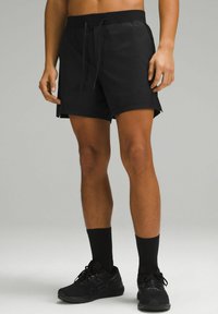 Shorts de sport noirs avec une taille élastique et un cordon de serrage, dotés d fentes sur les côtés et d'une texture lisse, accompagnés de chaussettes et de chaussures noires.
