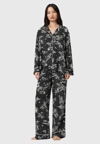 Zestaw piżamowy z czarnej tkaniny z białymi wzorami w kwiaty i gwiazdy. Długie rękawy, luźne spodnie i obszycia przy kołnierzy i mankietach.