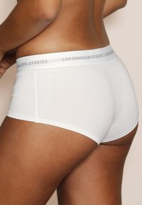Weiße Baumwoll-Boyshorts mit einem grauen Bund, der den Text "COPENHAGEN STUDIOS" trägt. Glatte Textur, enganliegendes Design.