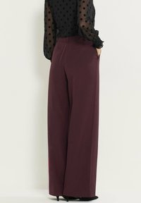 Wijde broekspijpen in bordeaux fabric, met een hoge taille, zijzakken en een soepele textuur. De achterkant toont een getailleerde pasvorm.
