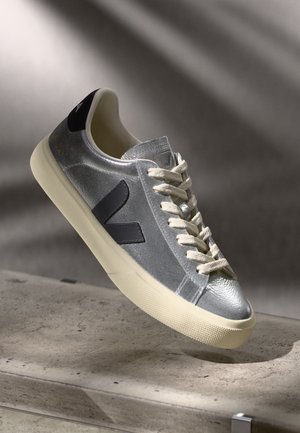 Grijze metallic sneaker met beige rubberen zool, witte veters, zwarte accenten en een gestructureerde afwerking. Heeft een opvallend 'V' logo aan de zijkant.