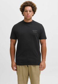 Sort t-shirt med korte ærmer lavet af bomuld og med en rund halsudskæring. Har hvid trykt tekst på venstre brystområde.