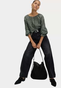Green floral blouse with puffed sleeves, high-waisted black jeans, and black perforated handbag. Black mules feature studded detail.