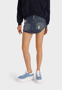 Sneakers azzurri chiari con lacci e suole bianche spesse, abbinati a una felpa scura e a una gonna di jeans strappata.