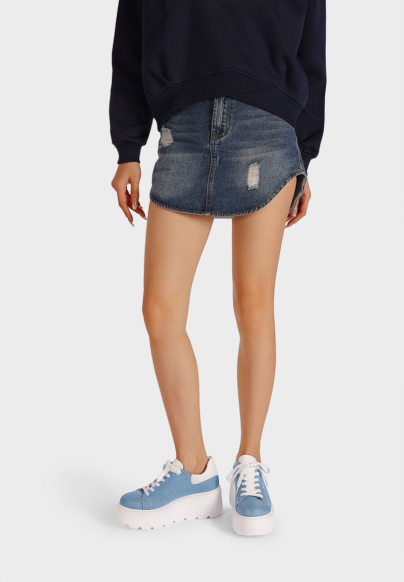 Sneakers azzurri chiari con lacci e suole bianche spesse, abbinati a una felpa scura e a una gonna di jeans strappata.