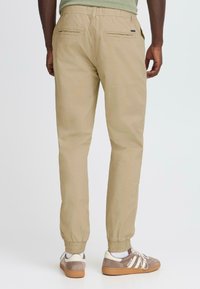 Pantalons de jogging beiges en tissu léger, dotés d'une taille élastique et de poignets en elastique, avec deux poches arrière et une texture lisse.