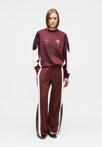Survêtement de sport bordeaux avec des accents crème ; le haut présente un col rond et un logo, tandis que le pantalon a des bandes latérales et une coupe décontractée.