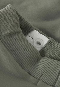 Col en tissu vert olive à texture côtelée, doté d'un bouton en plastique transparent et d'une étiquette cousue avec les instructions d'entretien.