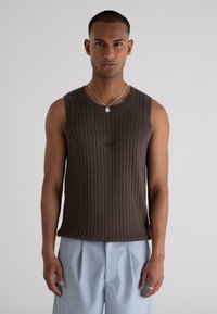 Brown ribbed sleeveless top with a round neckline and embroidered logo. Paired with light blue pleated trousers. Smooth texture.