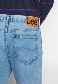 Vaaleansiniset farkut, joissa on nahkainen Lee-logopatchi takavyötäröllä, klassinen viisi-taskuinen muotoilu ja kontrast stitching.