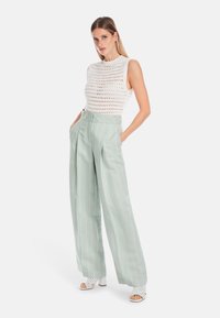 Weißes ärmelloses Strickoberteil mit offenem Gewebe, kombiniert mit hoch taillierten, mintgrünen gestreiften weit geschnittenen Hosen und weißen Absatzsandalen.