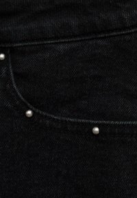 Tessuto di denim nero con una superficie liscia, impreziosito da borchie metalliche lungo la cucitura della tasca. Pattern di tessitura sottile visibile.