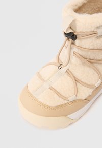Beige syntetisk vinterstøvle med fleece tekstur, snøresystem og gummisål. Har en polstret krave og diskrete syninger.