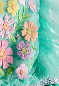 Türkisfarbener Stoff mit bestickten Blumen in Pink, Lavendel und Gelb; durchsichtige Textur, geraffte Kanten und silberne Verzierungen.