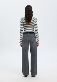 Szürke, bő szárú magas derekú farmernadrág fekete-fehér csíkos hosszú ujjú felsővel párosítva. A textúra simának és farmer anyagúnak tűnik.