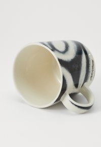 Taza de cerámica en blanco y negro con un patrón en espiral, forma cónica y asa lateral. El interior es de color crema sólido.