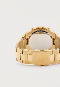 Zlata ura iz nerjavečega jekla z zapestnico iz členov, okroglim ohišjem, več pritisnimi gumbi in graviranim imenom blagovne znamke na zaponki.