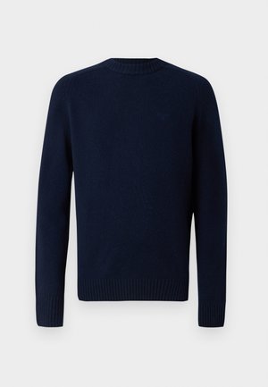 Navyblauwe gebreide trui met een ronde halslijn, geribbelde manchetten en zoom. Gladde textuur met een subtiel logo op de bovenrug. Eenvoudig ontwerp.