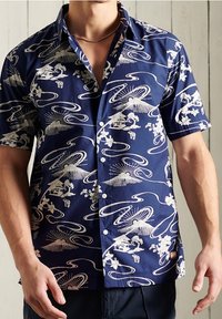 Camisa de manga corta en color marino con patrones florales y paisajísticos en blanco, confeccionada en tela ligera con un corte relajado y diseño de botones en la parte frontal.