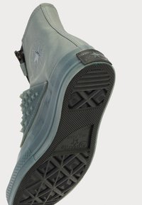 Converse Chuck de tom azul claro com uma superfície texturizada e detalhes em espinhos na lateral, apresentando uma sola de borracha preta e realces do logótipo.