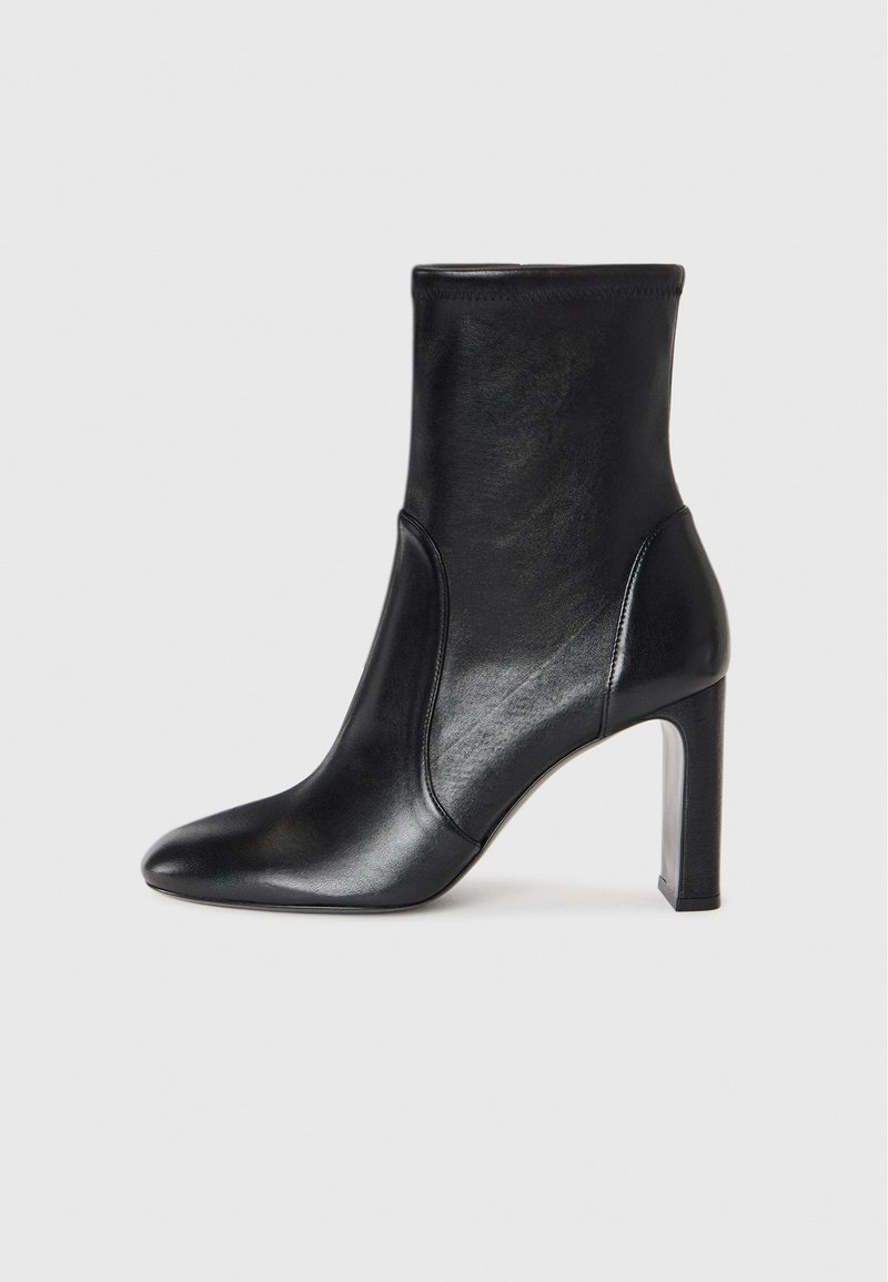 Bottine en cuir noir avec un design épuré, bout pointu et un haut talon carré. Présente une texture lisse et des détails de couture minimalistes.