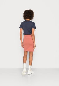 T-shirt azul-marinho combinado com uma saia rosa até ao joelho e botas brancas com solado grosso. A saia apresenta uma textura suave com uma cintura ajustada.