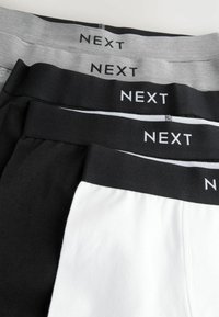 Trois paires de sous-vêtements pour hommes avec des ceintures élastiques. Les couleurs incluent le noir, le blanc et le gris, chacune étiquetée "NEXT" dans une police contrastante.