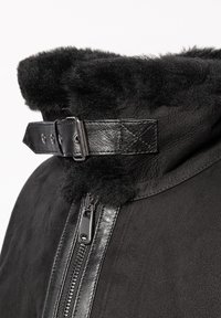 Schwarze Wildlederjacke mit einem weichen schwarzen Lammfellkragen, ausgestattet mit einem Reißverschluss und einem Lederriemen zur Anpassung.