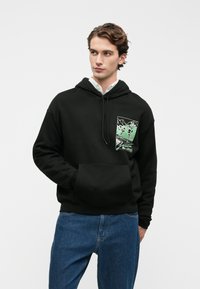 Hanorac negru cu buzunar frontal și un design grafic în verde care înfățișează munți. Fabricat dintr-un material moale, cu o croială lejeră și glugă cu șnur.